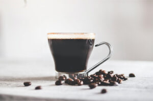 Cup of black coffee on a table surrounded by coffee beans.