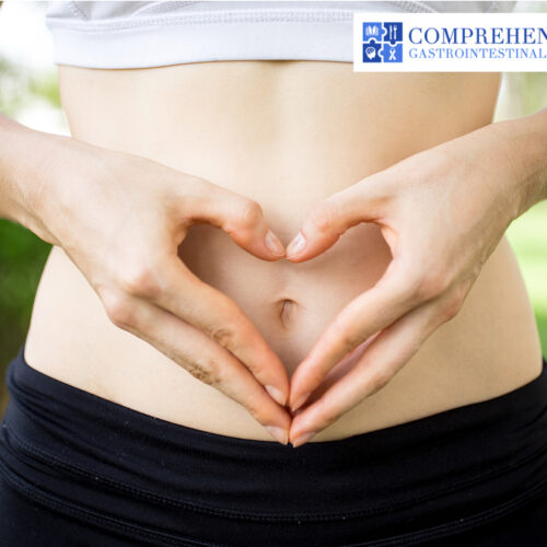 Woman making a heart shape with her hands on her stomach.